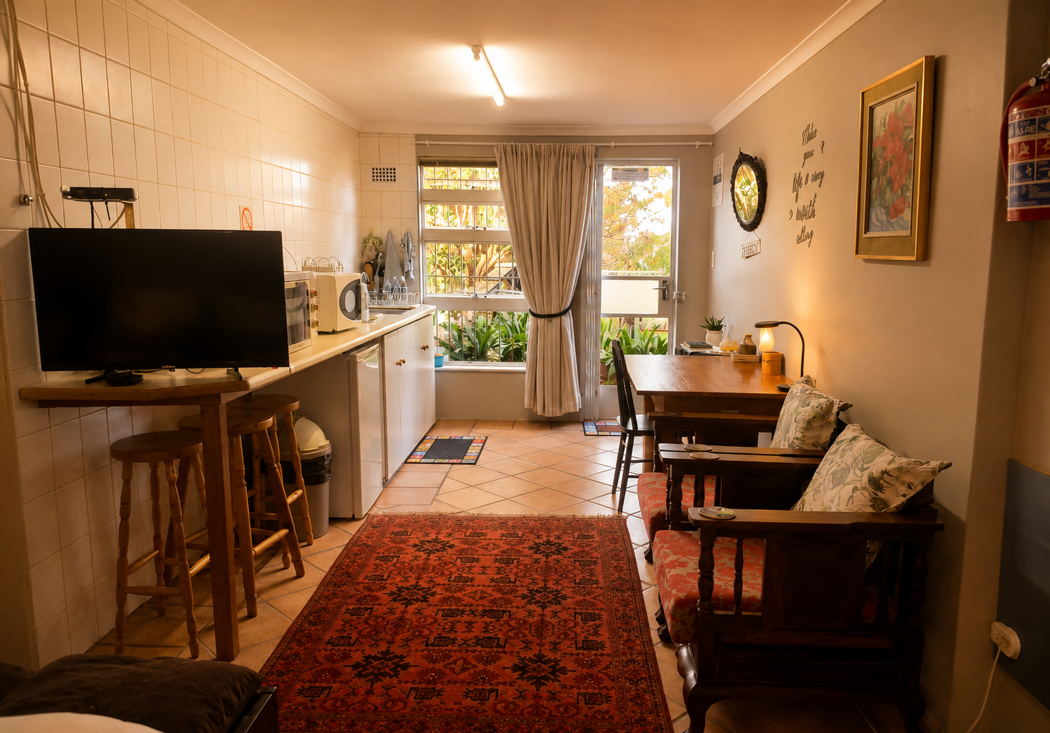Hibiskus Suite living area with kitchenette, TV, writing desk, garden door and lounge chair